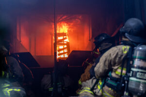 Flames climb as firefighters wait inside of the Flashover Training Simulator