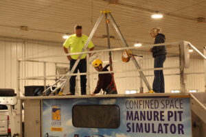 Dan Neenan provides instruction to Landon Grove, agriculture science student, as he is lowered into the manure pit simulator.