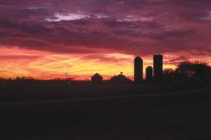 Photo of sunset behind farm with silos and a wind turbine visible